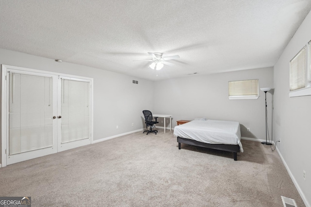 carpeted bedroom featuring a textured ceiling, baseboards, a ceiling fan, and visible vents