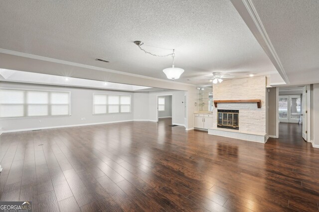 unfurnished living room featuring ceiling fan, a fireplace, a textured ceiling, ornamental molding, and visible vents