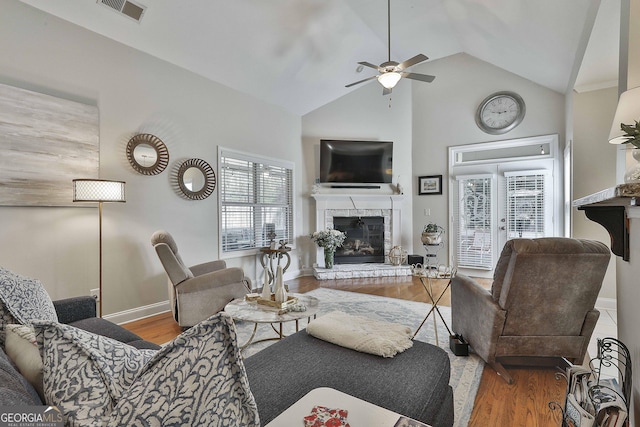 living room with ceiling fan, a glass covered fireplace, visible vents, wood finished floors, and baseboards