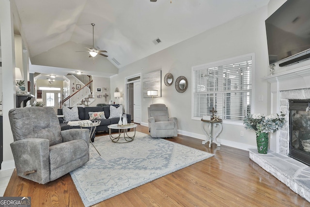 living area with a glass covered fireplace, stairs, visible vents, ceiling fan, and wood finished floors