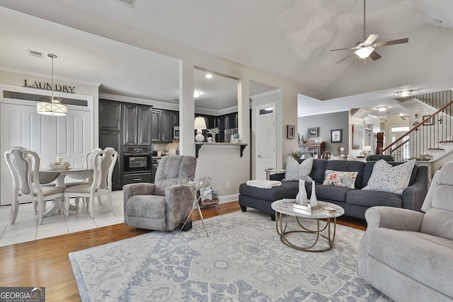 living room featuring ceiling fan, light wood-type flooring, ornamental molding, vaulted ceiling, and stairs