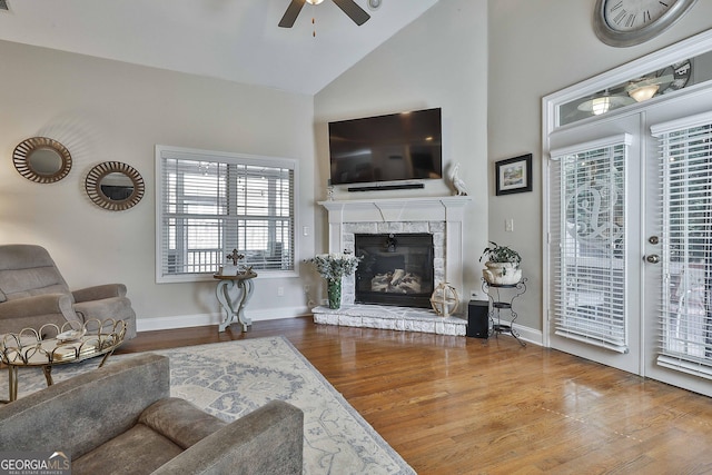 living area with baseboards, a stone fireplace, ceiling fan, high vaulted ceiling, and wood finished floors