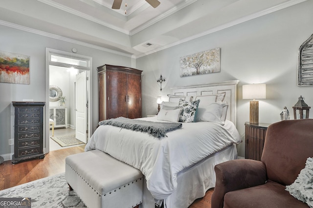 bedroom with ornamental molding, connected bathroom, a tray ceiling, ceiling fan, and wood finished floors