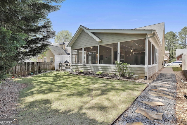 rear view of house featuring a yard, fence, a sunroom, and a ceiling fan