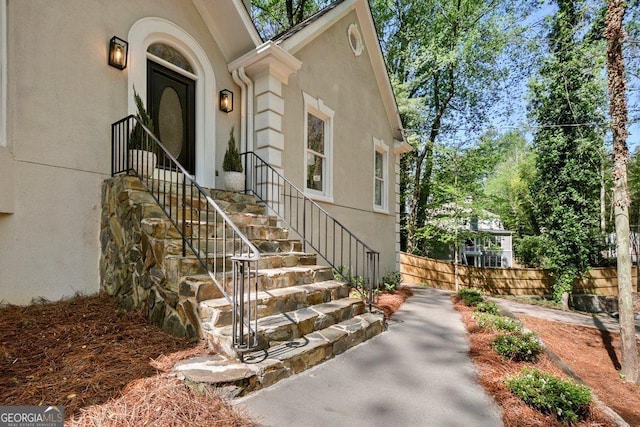 doorway to property featuring stucco siding and fence