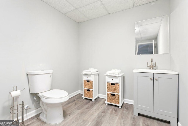 half bath featuring toilet, a paneled ceiling, wood finished floors, baseboards, and vanity