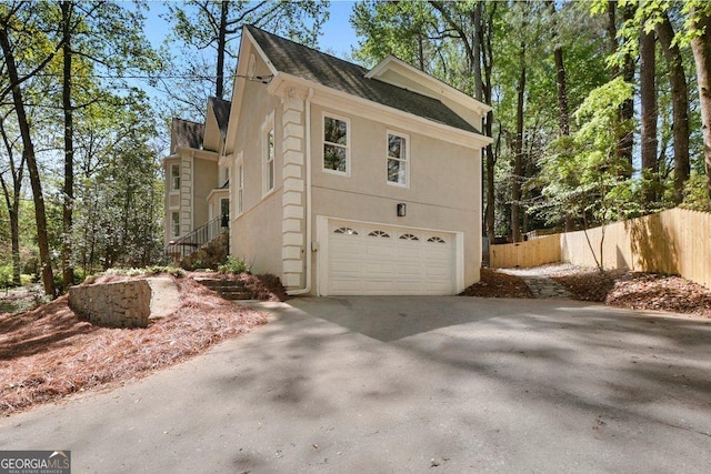 view of side of property featuring a garage, concrete driveway, fence, stucco siding, and stairs