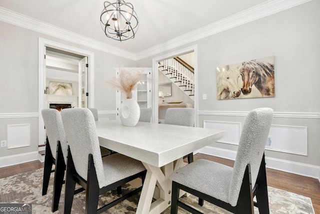 dining area featuring a chandelier, stairway, crown molding, wood finished floors, and a lit fireplace