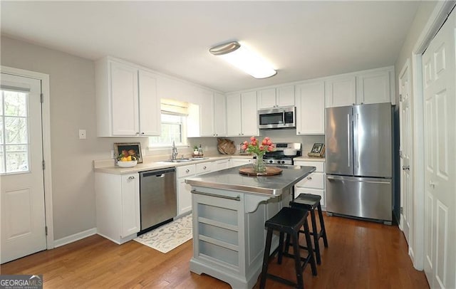 kitchen featuring a kitchen breakfast bar, white cabinets, appliances with stainless steel finishes, wood finished floors, and a sink