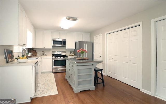 kitchen with appliances with stainless steel finishes, white cabinetry, a kitchen island, dark wood finished floors, and a sink