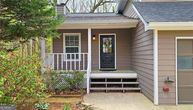 property entrance with roof with shingles, a chimney, and covered porch