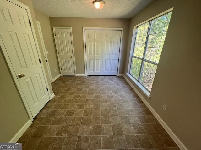 unfurnished bedroom featuring baseboards, a textured ceiling, and multiple windows