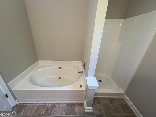 bathroom featuring baseboards, a bath, and a stall shower