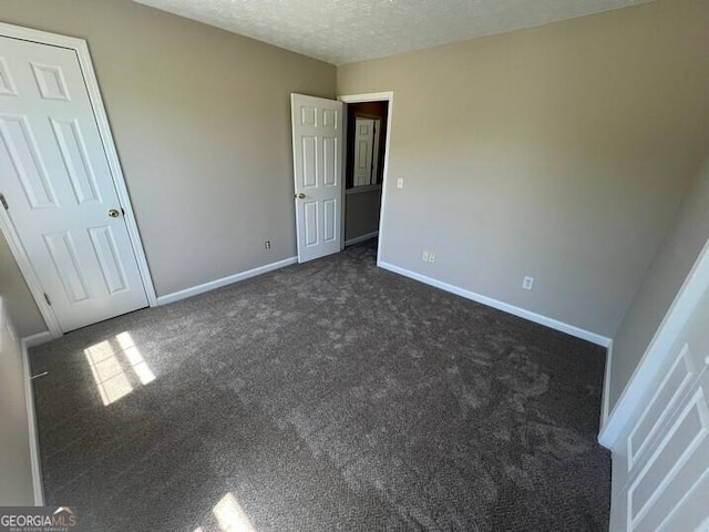 unfurnished bedroom featuring baseboards, dark carpet, and a textured ceiling