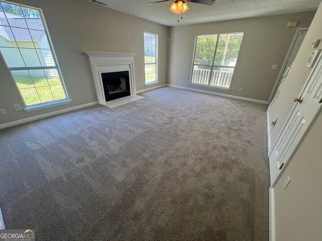unfurnished living room with a fireplace with flush hearth, ceiling fan, carpet, baseboards, and visible vents