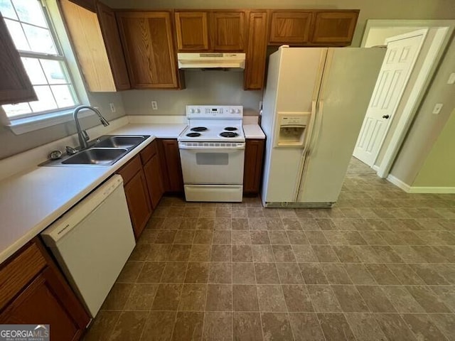 kitchen with a sink, brown cabinets, white appliances, light countertops, and under cabinet range hood
