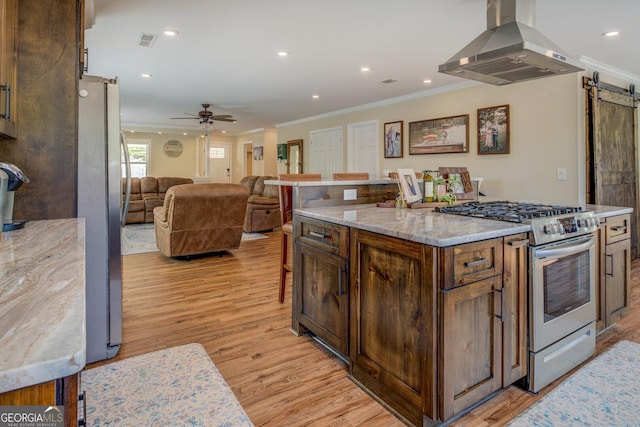 kitchen featuring a barn door, stainless steel appliances, visible vents, island range hood, and ornamental molding