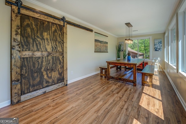 dining area with a barn door, wood finished floors, ornamental molding, baseboards, and a notable chandelier