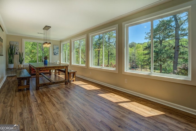 sunroom featuring baseboards, crown molding, and wood finished floors