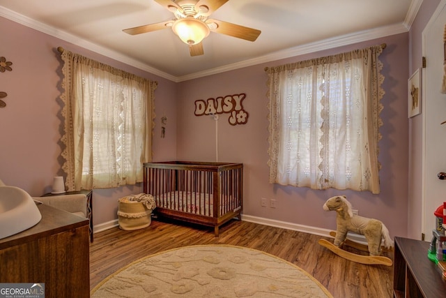 bedroom with crown molding, wood finished floors, a crib, and multiple windows
