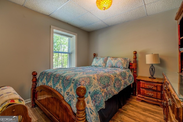 bedroom featuring a paneled ceiling, baseboards, and wood finished floors