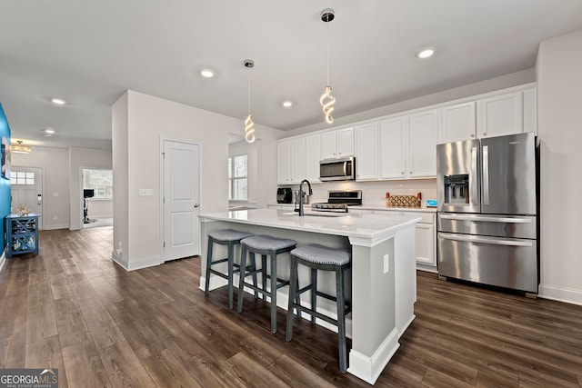 kitchen with a kitchen island with sink, a sink, stainless steel appliances, backsplash, and light countertops