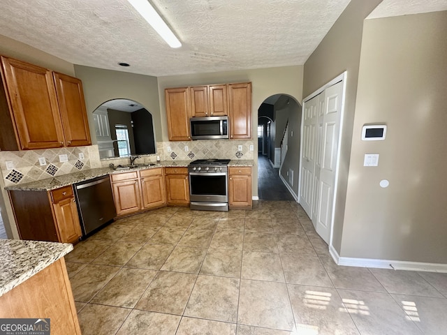 4254 Wood Cove Dr, Snellville, GA 30039 - kitchen featuring tasteful backsplash, arched walkways, a sink, light stone countertops, and stainless steel appliances