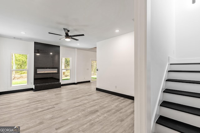 unfurnished living room featuring baseboards, a ceiling fan, a fireplace, stairway, and wood finished floors