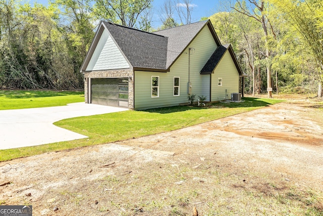 view of home's exterior with central AC unit, a yard, stone siding, driveway, and roof with shingles