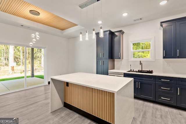 kitchen featuring light wood-style flooring, light countertops, backsplash, a kitchen island, and a sink