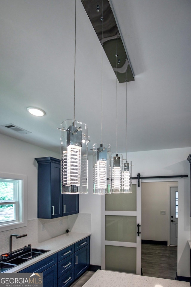kitchen with light countertops, blue cabinetry, a barn door, visible vents, and a sink