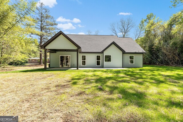 back of property with a patio, a shingled roof, and a lawn
