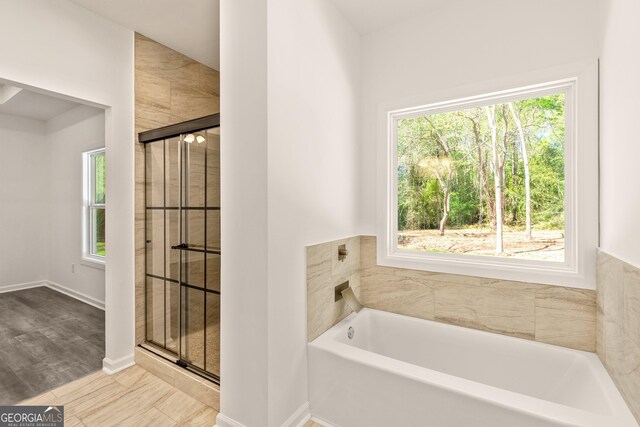 bathroom featuring a bath, wood finished floors, baseboards, and plenty of natural light