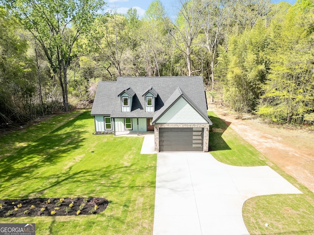 new england style home featuring driveway, stone siding, an attached garage, a front lawn, and a shingled roof