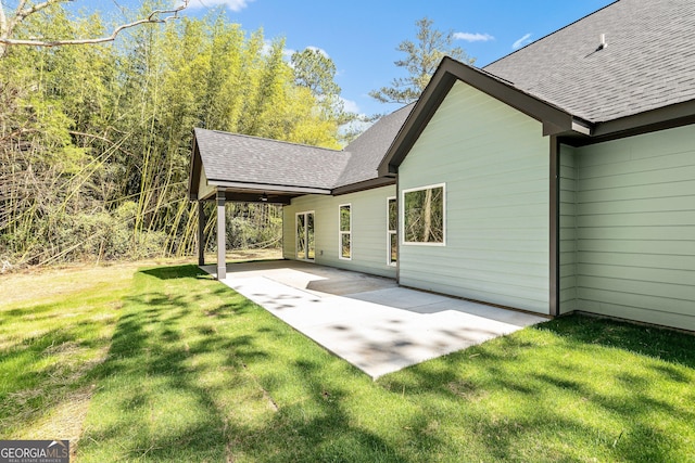 back of property featuring a patio, roof with shingles, and a lawn