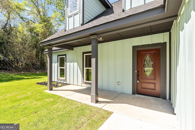 entrance to property featuring board and batten siding, a yard, and a shingled roof