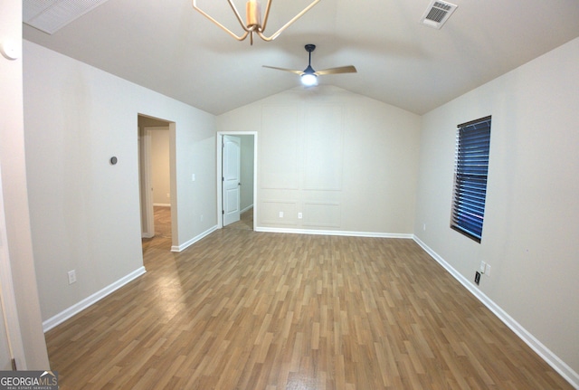 empty room with ceiling fan with notable chandelier, visible vents, wood finished floors, lofted ceiling, and baseboards