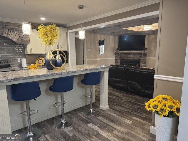 kitchen featuring a breakfast bar, a fireplace, white cabinetry, crown molding, and dark wood-type flooring