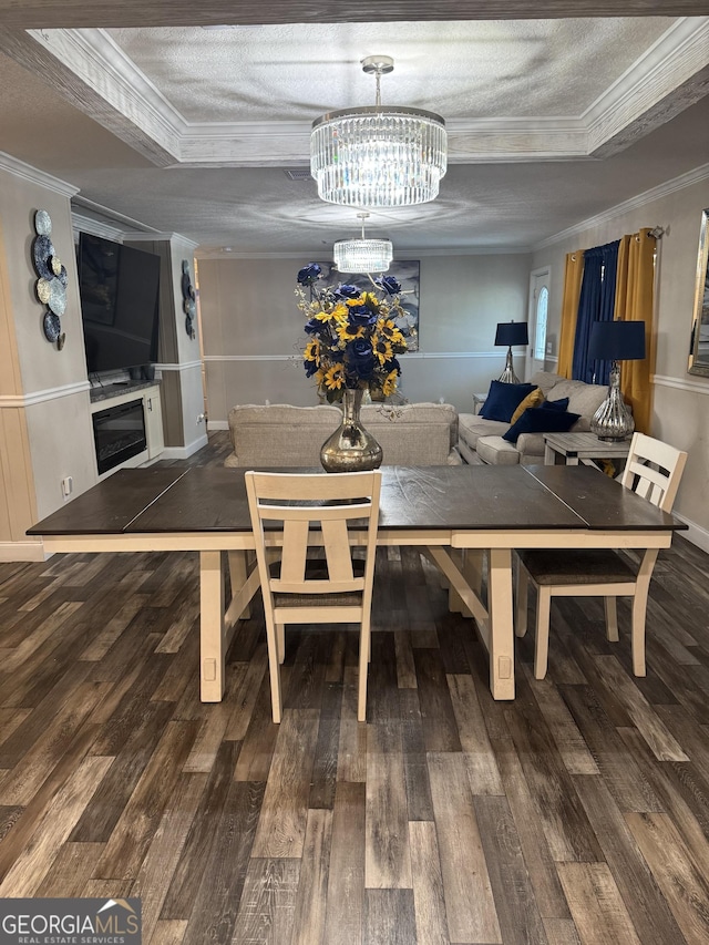 dining area featuring a notable chandelier, a tray ceiling, crown molding, and wood finished floors