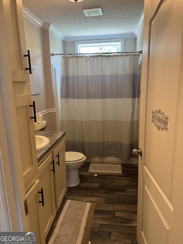 full bath featuring vanity, ornamental molding, a textured ceiling, visible vents, and wood finished floors