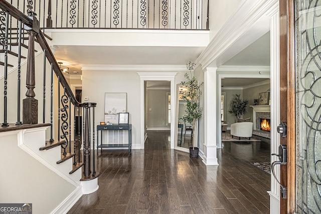 entrance foyer with baseboards, a lit fireplace, wood finished floors, stairway, and ornamental molding