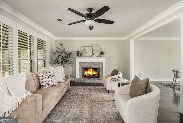 living room with a brick fireplace, visible vents, ceiling fan, and crown molding