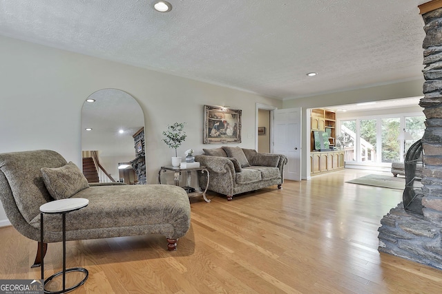 living area featuring ornamental molding, a fireplace, recessed lighting, a textured ceiling, and light wood finished floors