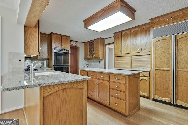 kitchen with a peninsula, dobule oven black, a sink, and light wood finished floors