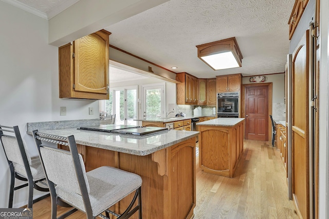 kitchen with brown cabinetry, crown molding, a peninsula, light wood-style floors, and stainless steel appliances
