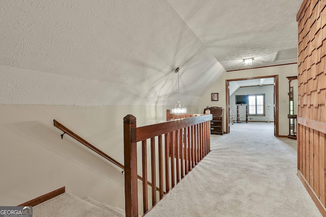 hall featuring light colored carpet, a textured ceiling, baseboards, an upstairs landing, and vaulted ceiling
