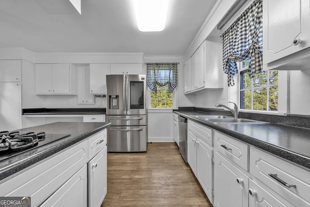 kitchen with appliances with stainless steel finishes, a sink, white cabinetry, and dark countertops