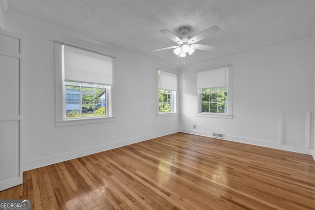 empty room featuring hardwood / wood-style floors, ceiling fan, visible vents, and a textured ceiling