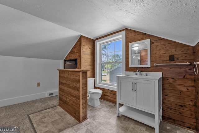 bathroom with vanity, wooden walls, a textured ceiling, toilet, and lofted ceiling