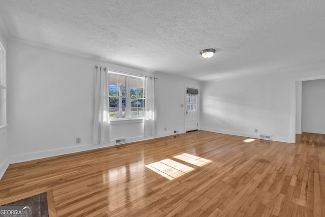 unfurnished living room with light wood-style flooring, a textured ceiling, baseboards, and visible vents